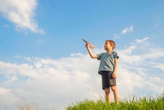 Little boy launches a paper plane into the air. Child launches a paper plane. Happy kid playing with paper airplane.