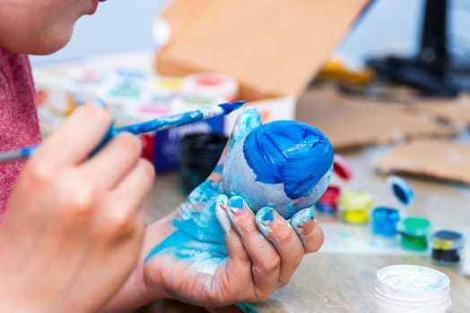 Kid is dyeing Easter eggs. The boy is sitting at the table and enthusiastically engaged in creativity, preparing for Easter.