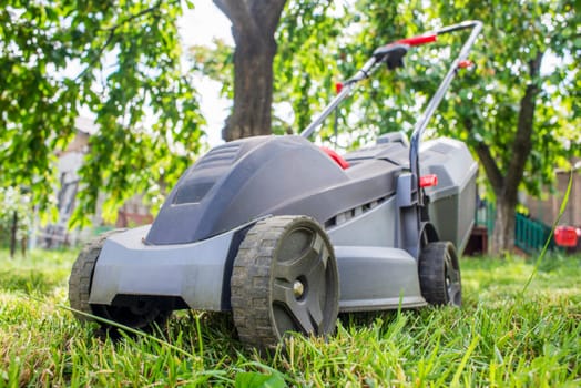 Lawn mower on a lawn on a background of trees. Outdoor shot of lawnmower.