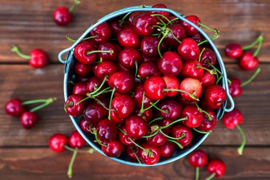 Fresh red ripe cherry in a bucket on the wooden background, top view. Ripe red cherries in the metal bucket on a wooden background.