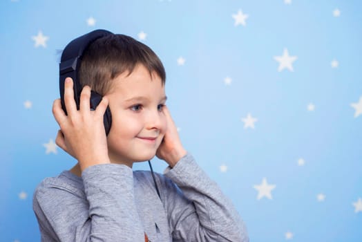 Happy smiling child enjoys listens to music in headphones on blue background with stars. A boy listening to music on headphones.