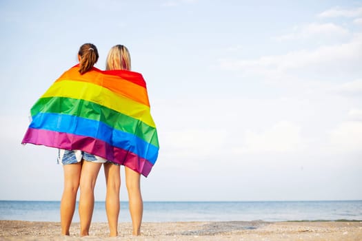 Lesbian couple holding lgbt flag and hugging outdoors. LGBT rainbow flag.