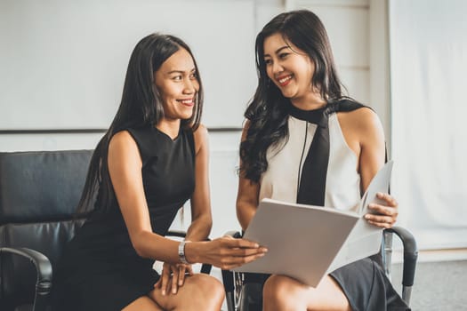 Two businesswomen discussing business while looking at financial data in their hands. They are sitting on the chairs in the office meeting room. uds