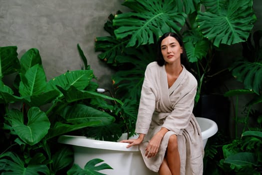 Tropical and exotic spa garden with bathtub in modern hotel or resort with young woman in bathrobe enjoying leisure and wellness lifestyle surrounded by lush greenery foliage background. Blithe