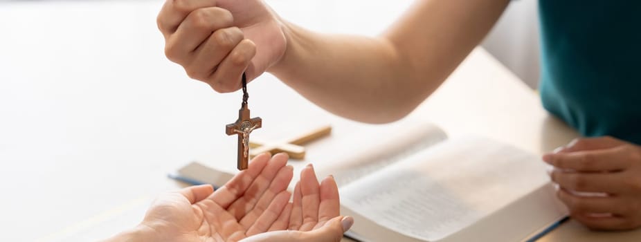 Close-up women prayer deliver holy bible book and holy cross to young believer. Spreading religion symbol. Concept of hope, religion, christianity and god blessing. Warm background. Burgeoning.