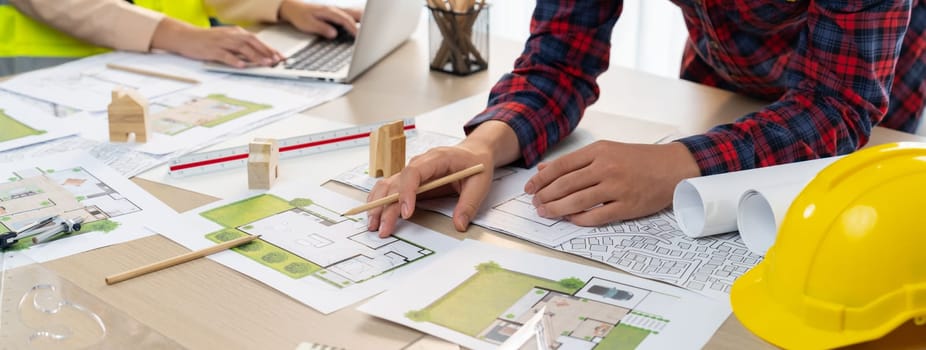 A cropped portrait of professional architect working with blueprint during safety engineer using laptop analysis data at meeting table with document scatter around. Close up. Delineation.