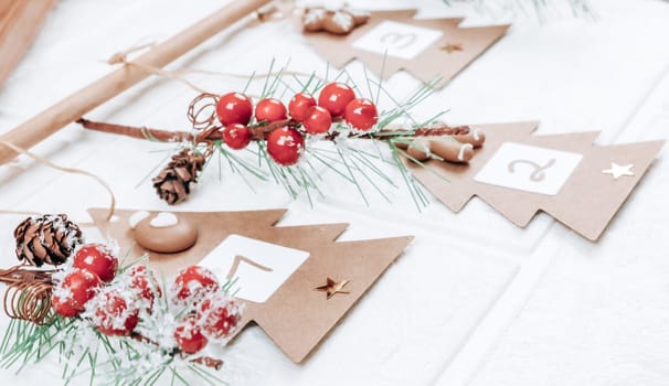 Three handicraft Christmas trees with numbers 1,2,3, cookies and spruce branches hang on a jute thread and on a hanger on a white brick wall, close-up side view. Advent calendar concept.