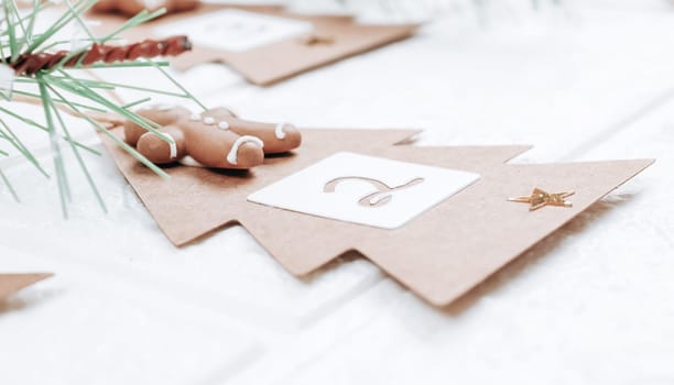 One handicraft Christmas tree with numbers 2, biscuits and fir branches hang on a jute thread and on a hanger on a white brick wall, close-up side view. Advent calendar concept.