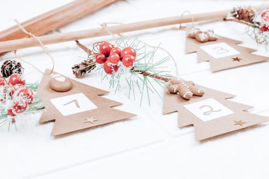 Craft Christmas trees with numbers 1,2,3 and fir branches with red berries hang on a wooden hanger on a white brick wall, close-up side view. Advent calendar concept.