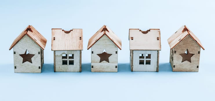 Five wooden houses with windows and stars lie in an even row on a light blue background, close-up side view. Concept of natural toys, Christmas.