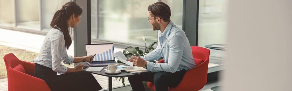 Two coworkers working together on project while using laptop in office meeting room