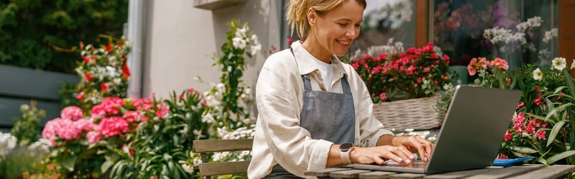 Beautiful flower shop owner wearing apron working on laptop in her store