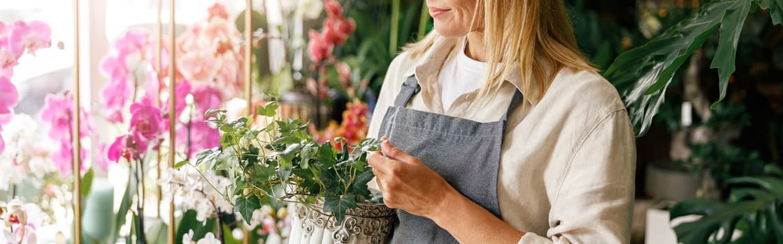 Woman florist small business owner standing in floral store and waiting for client with houseplants