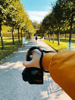 In a park, amidst trees, a man photographs a girl walking on a path, showcasing a first-person viewpoint. pov