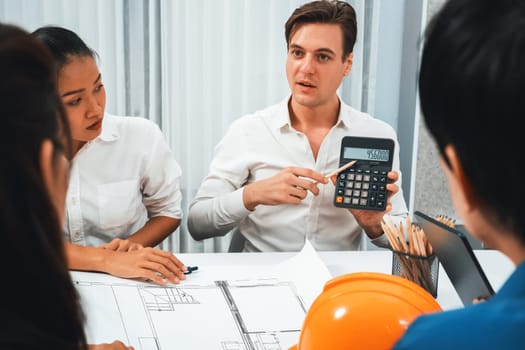 Diverse group of civil engineer and client working together on architectural project, building blueprint and calculate risk reduction for construction project at meeting table. Prudent