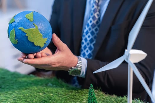 Eco business and save Earth concept shown by businessman or CEO holding paper globe in office with eco friendly mockup to promote CO2 and carbon footprint reduction for greener future. Quaint