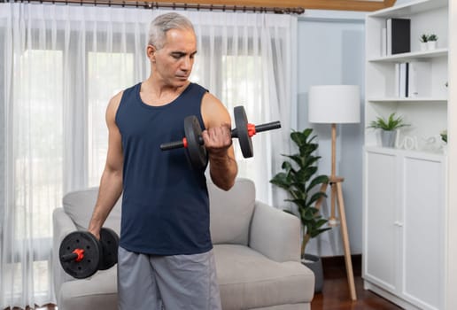 Athletic and sporty senior man engaging in body workout routine with lifting dumbbell at home as concept of healthy fit body with body weight lifestyle after retirement. Clout