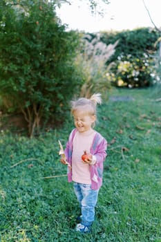 Little girl with a pomegranate and a yellow leaf in her hands stands in the garden. High quality photo