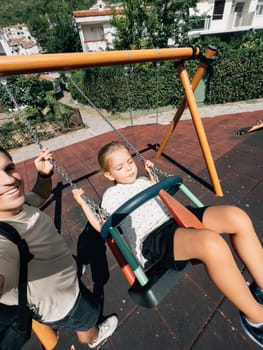 Dad swings a little girl on a chain swing at the playground. High quality photo