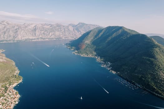 Yachts sail along the Bay of Kotor against the backdrop of a green mountain range. Montenegro. Drone. High quality photo