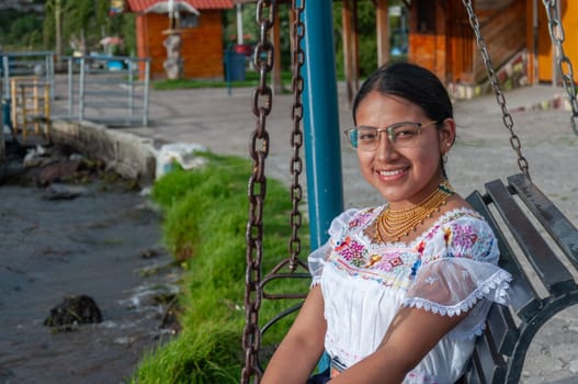 indigenous woman with glasses looking at camera very smiling sitting on a swing next to a lagoon. glasses day. High quality photo