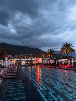 Sun loungers with folded umbrellas stand near the illuminated pool at dusk. High quality photo