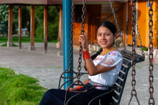 copy space of an indigenous girl looking at the camera smiling sitting on a swing next to a wooden house. High quality photo