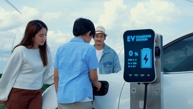 Modern family travel and nature with eco-friendly EV car concept, recharging battery from charging station using renewable energy from wind turbine for future energy sustainability. Peruse