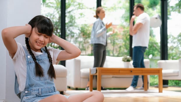 Stressed and unhappy girl huddle in corner, cover her ears with painful expression while her parent arguing in background. Domestic violence and traumatic childhood depression. Panorama Synchronos