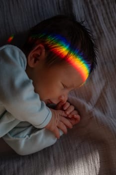 Close-up portrait of a newborn boy with a prism beam on his face. Rainbow