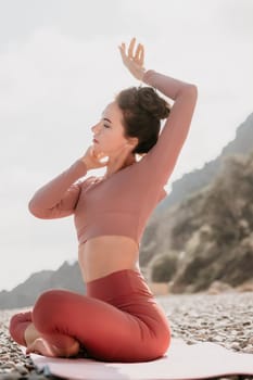 Young woman with long hair in white swimsuit and boho style braclets practicing outdoors on yoga mat by the sea on a sunset. Women's yoga fitness routine. Healthy lifestyle, harmony and meditation