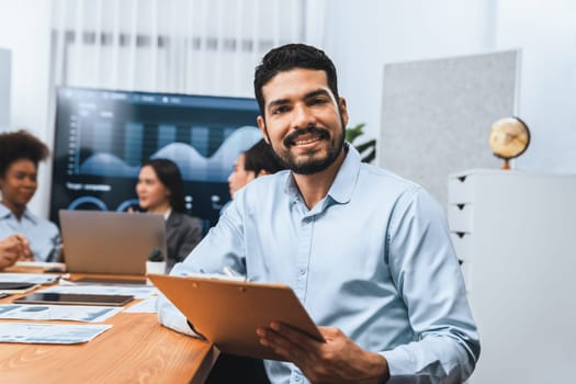 Portrait of happy and smiling businessman with group of coworkers on meeting with screen display business dashboard in background. Confident office worker at team meeting. Concord