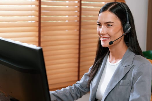 Female call center operator or customer service helpdesk staff working on workspace while talking on the headset to provide assistance for customer. Professional modern business service. Blithe