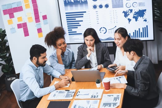 Multiracial analyst team use BI dashboard data to analyze financial report on meeting table. Group of diverse business people utilize data analysis by FIntech for success business marketing. Concord