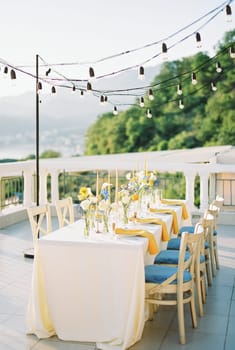 Festive table with bouquets of flowers stands on a terrace with garlands of light bulbs on stands. High quality photo