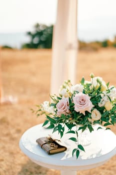 Wedding rings lie on a book on the reception table near a bouquet of flowers on the lawn. High quality photo