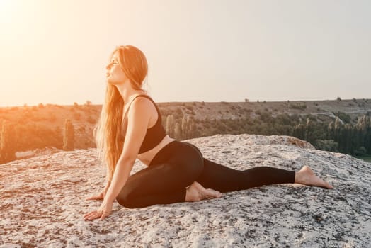 Well looking middle aged woman with long hair, fitness instructor in leggings and tops doing stretching and pilates on the rock near forest. Female fitness yoga routine concept. Healthy lifestyle.