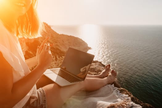 Woman sea laptop. Business woman in yellow hat working on laptop by sea. Close up on hands of pretty lady typing on computer outdoors summer day. Freelance, digital nomad, travel and holidays concept.