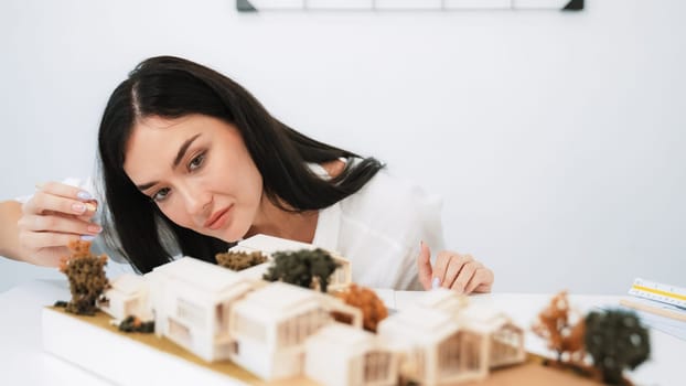 Closeup portrait image of young beautiful architect focus on measures the architectural model with blueprint placed on table in modern meeting room. Creative business design concept. Immaculate.