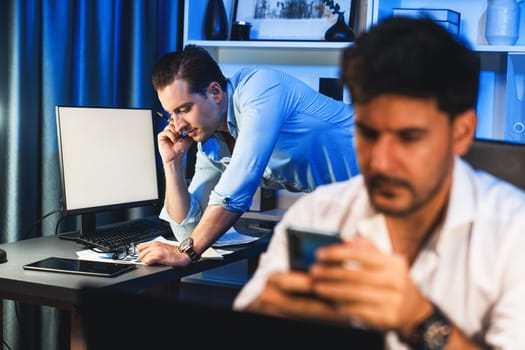 Colleagues concentrating on their job task at night home office behind desk while another man with thoughtful face solving to postpone the deadline of project at the blurred front side. Sellable.