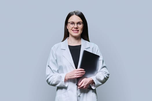 Portrait of young woman specialist, professional medical scientist, pharmacist in white coat with laptop on grey background. Medical staff, occupation, health care, science medicine, online services