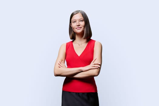 Portrait of young confident woman in red on white studio background. Successful fashionable female with crossed arms looking at camera. Business, work, services, education, fashion beauty professions