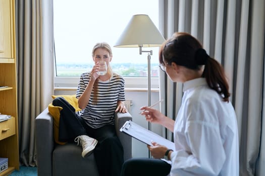 Young female teenager 16, 17 years old talking with counselor psychologist behavior social worker teacher, sitting in chair in office. Psychology psychotherapy therapy mental health adolescence youth