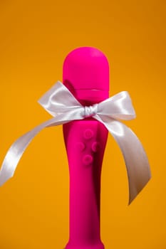 Pink vibrator with a white bow on an orange background. Women's gift