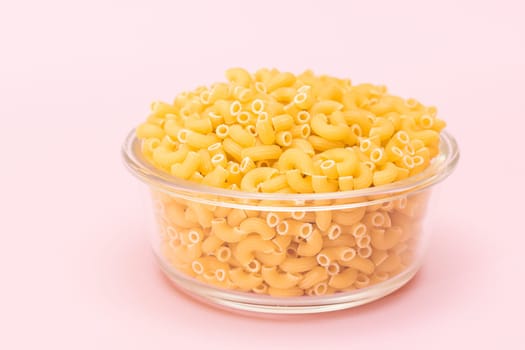 Uncooked Chifferi Rigati Pasta in Glass Jar on Pink Background. Fat and Unhealthy Food. Classic Dry Macaroni. Italian Culture and Cuisine. Raw Pasta