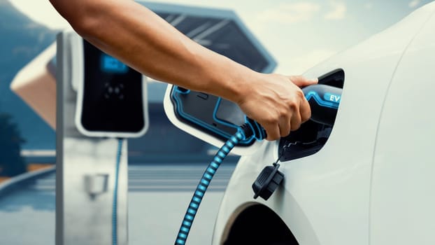 Asian man insert EV charger and recharge his electric car recharging energy from future home charging station. Smart and futuristic home energy infrastructure. Peruse