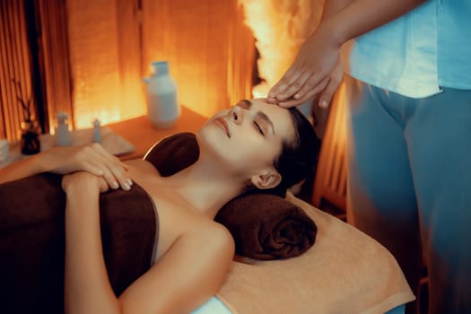 Caucasian woman enjoying relaxing anti-stress head massage and pampering facial beauty skin recreation leisure in warm candle lighting ambient salon spa in luxury resort or hotel. Quiescent