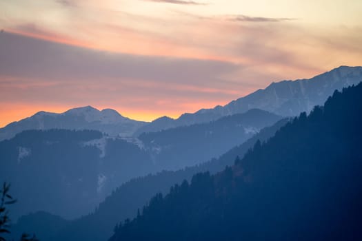 red orange dusk dawn colors over snow covered himalaya mountains and fluffy clouds showing hill stations in jhibbi kullu manali India