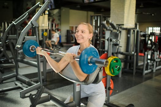 Woman training biceps with a barbell in the gym. Strength training with heavy equipment.