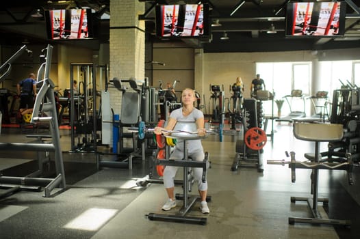 Woman training biceps with a barbell in the gym. Strength training with heavy equipment.